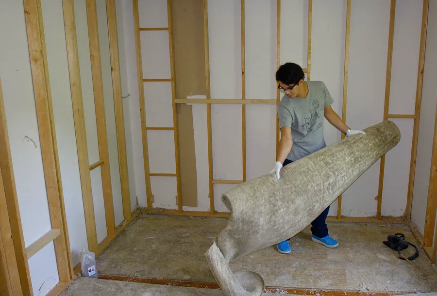 Worker rolling up old carpet in a gutted bedroom during a remodel