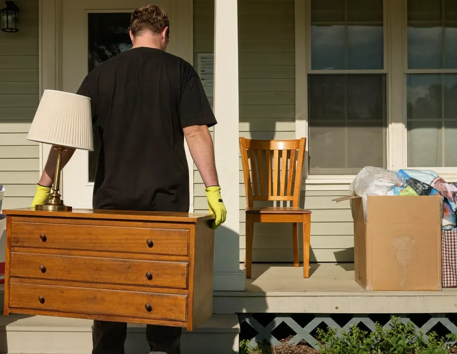 Worker carrying a good wooden chair and a box of household goods to the trailer for donation