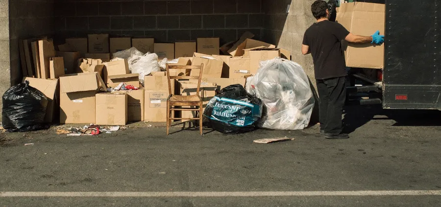 Worker loading overflow trash and cardboard from a dumpster enclosure into a trailer
