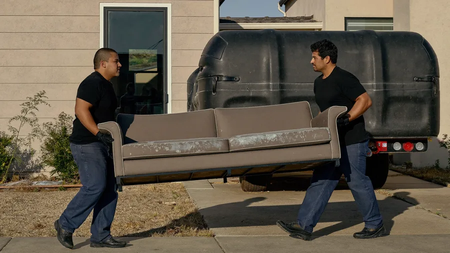 Two Those Junk Movers workers carrying an old couch to the trailer in a Fresno driveway