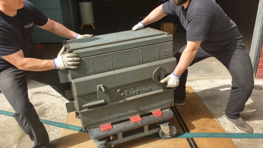 Two workers tipping a heavy gun safe onto a heavy-duty dolly in a garage